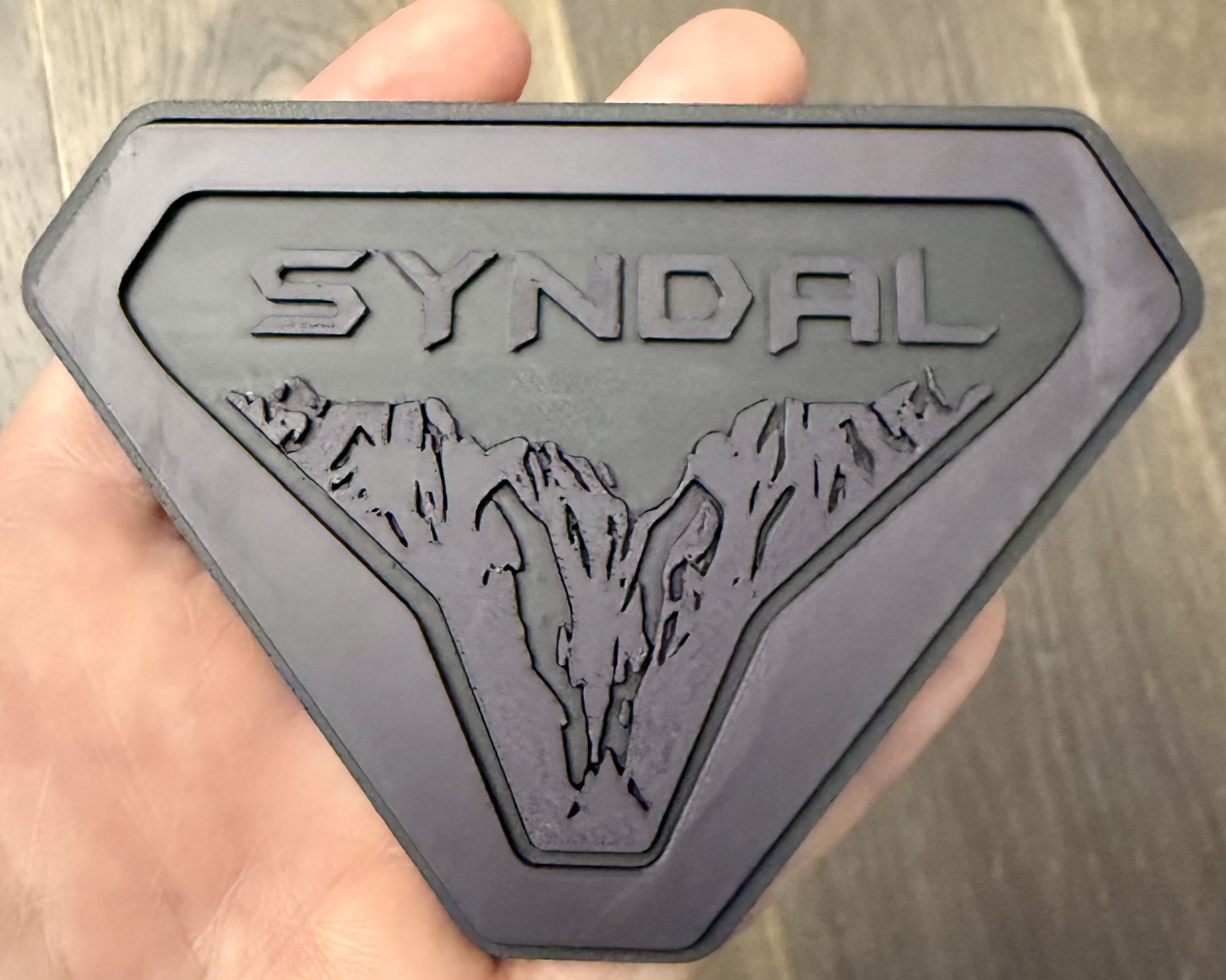 Dark gray Syndal badge held in hand